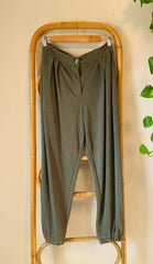 Green pants hanging on a bamboo rack against a beige wall.