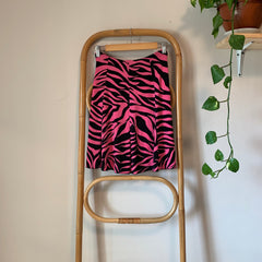 Pink and black zebra-patterned  skirt on a wooden ladder against a white wall with greenery.