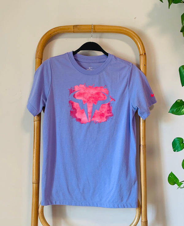 Purple t-shirt with pink floral design on a hanger against a beige wall.