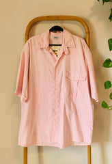 Pink shirt on a hanger against a beige wall with green leaves.