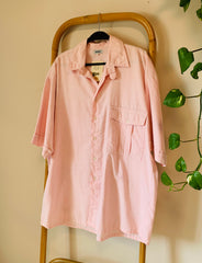Pink shirt on a hanger against a beige wall with a plant in the corner